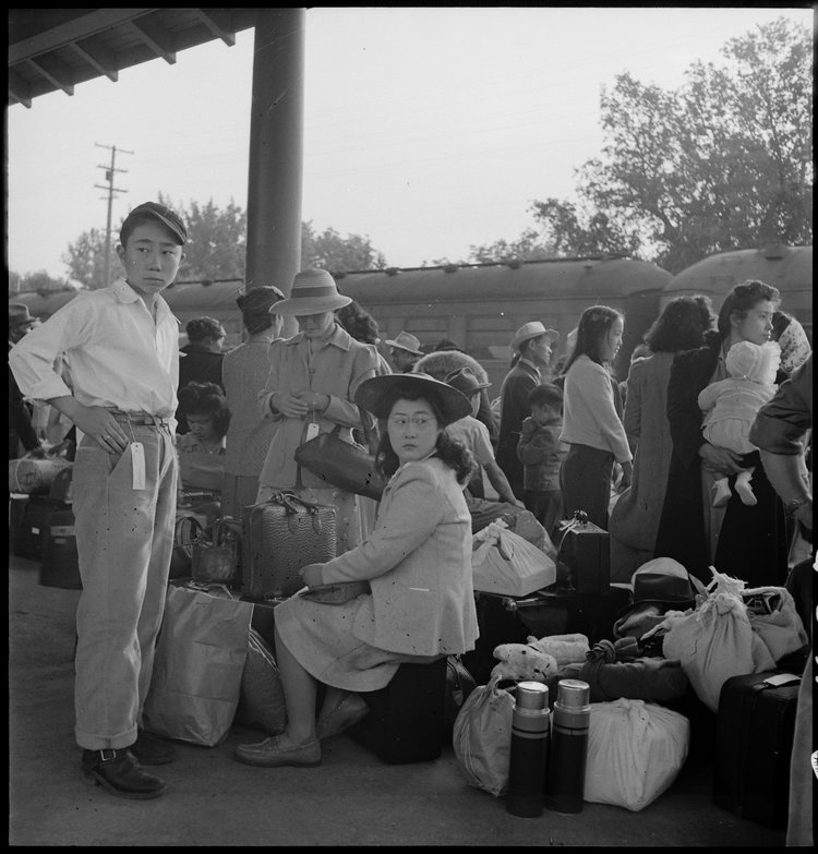 Woodland, California. Families of Japanese ancestry with their baggage at railroad station awaiting the arrival of special train which will take them to the Merced Assembly center, 125 miles away.