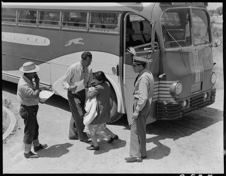 Stockton, California. Young mother of Japanese ancestry has just arrived at this Assembly center with her baby and she is the last to leave the bus. Her identification number is being checked and she will then be directed to her place in the barracks after preliminary medical examination.